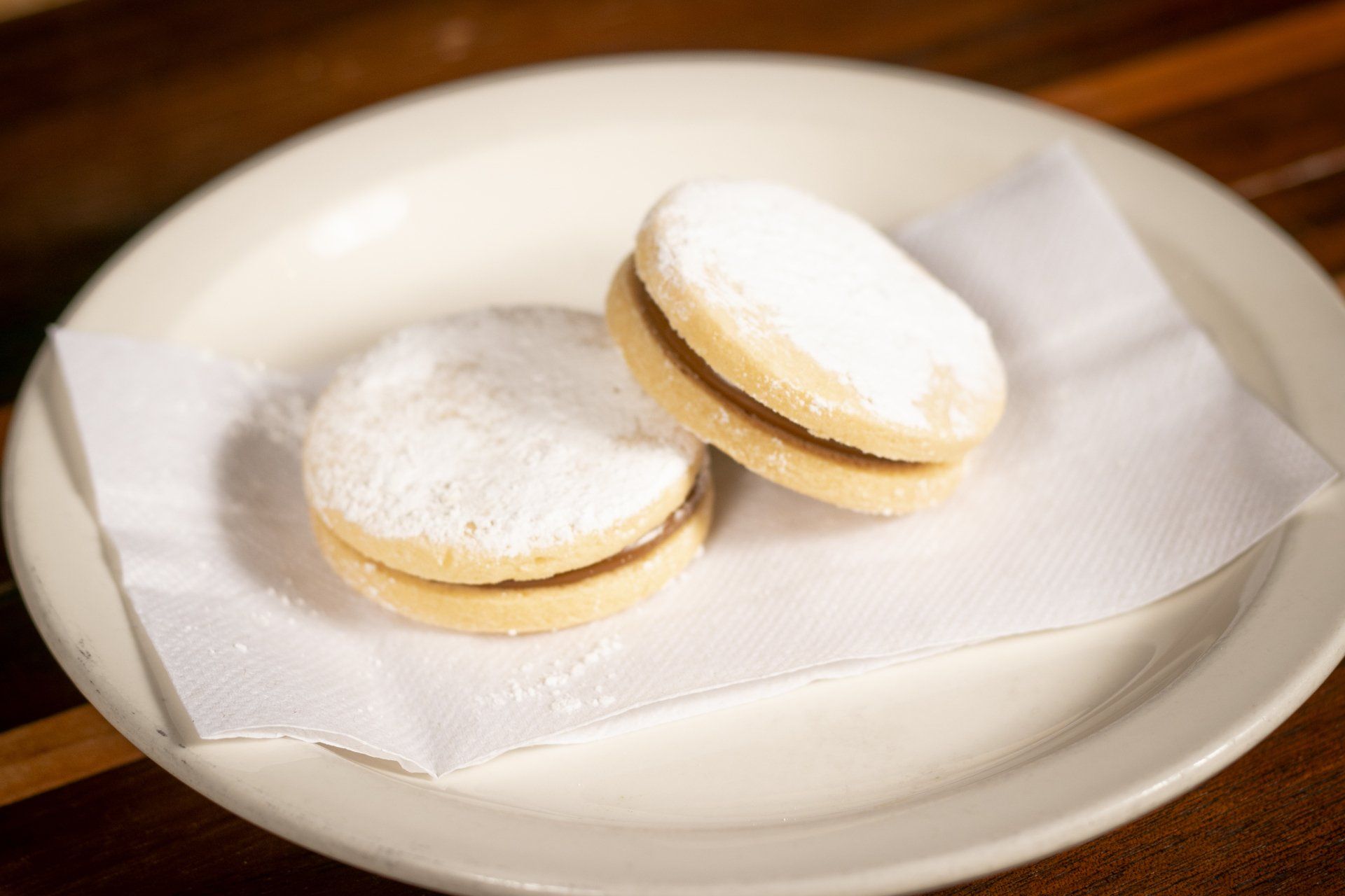 Two alfajores cookies on a white plate, dusted with powdered sugar.