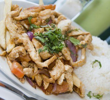 Sautéed chicken with onions, tomatoes, and fries, served with white rice, garnished with cilantro.