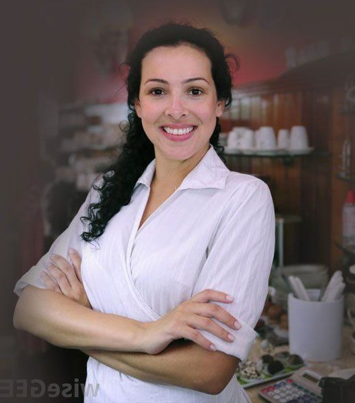 Woman with arms crossed smiling in a restaurant. She wears a white shirt, behind a counter.