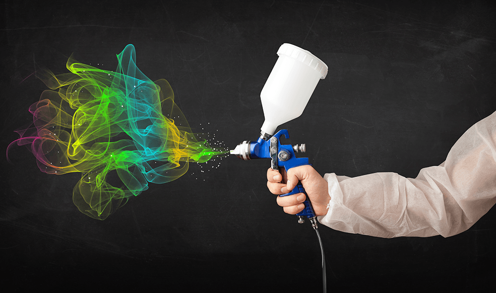 Hand holding a paint sprayer, spraying colorful paint against a dark background.