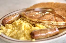 A close up of a plate of food with pancakes , eggs and sausage