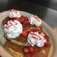 A plate of pancakes with whipped cream and strawberries on top