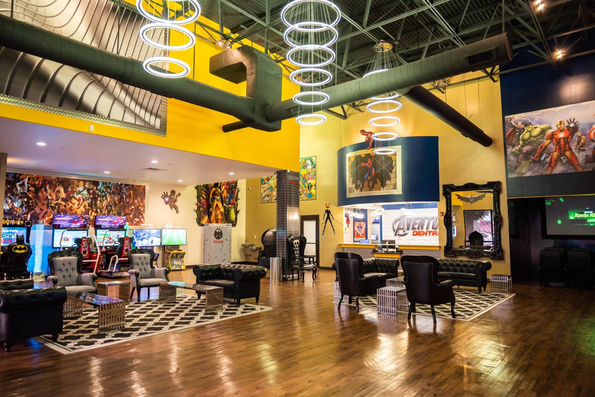 Modern lounge with wood floors, colorful art, ring lights, arcade machines, and tables in a spacious room