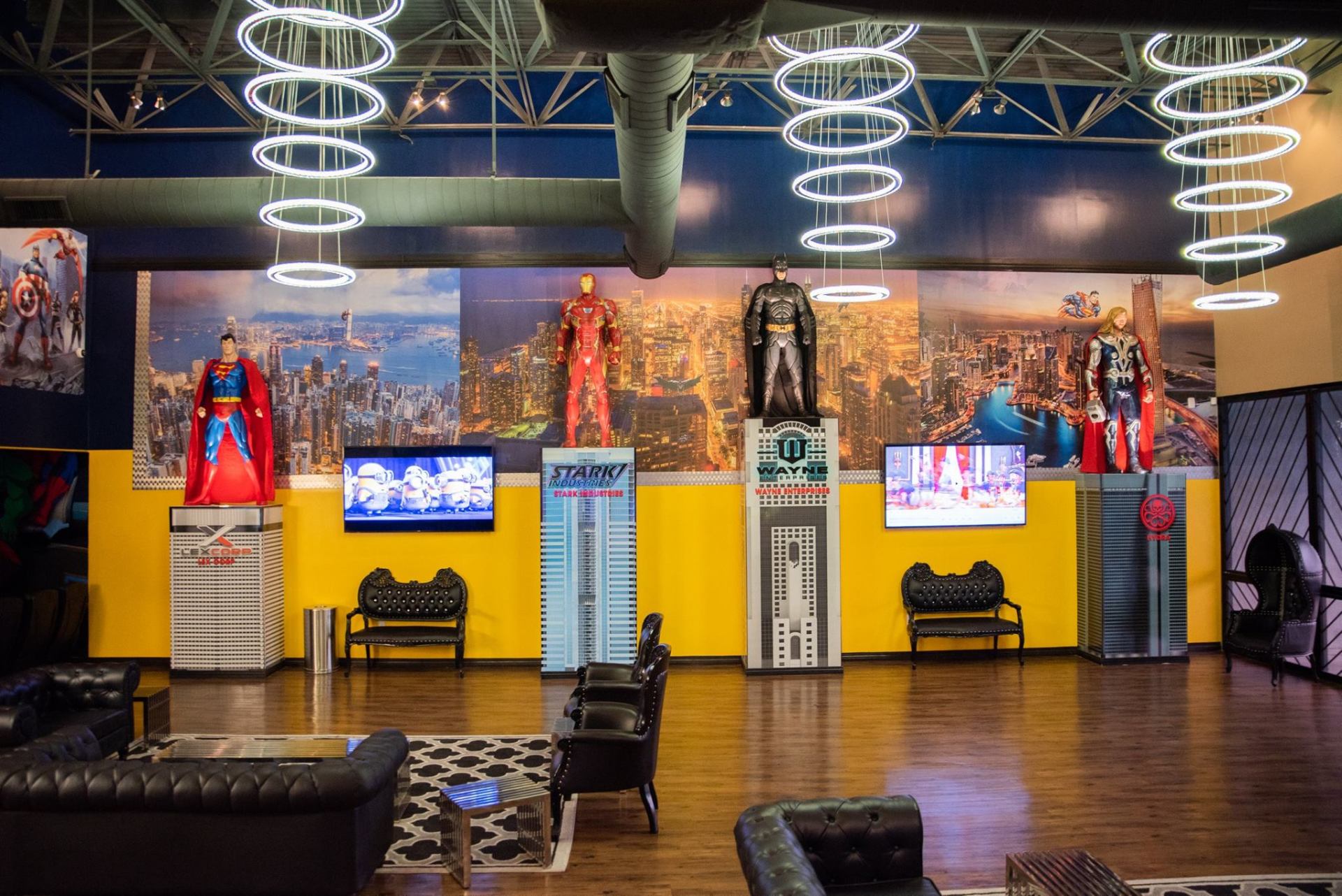 Colorful museum exhibit with superhero mannequins, yellow walls, TV screens, and spiral ceiling lights