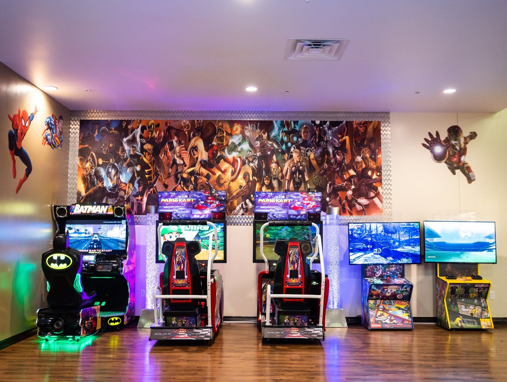Arcade room with glowing game cabinets lined against a wall mural, colorful lights on wood floors.