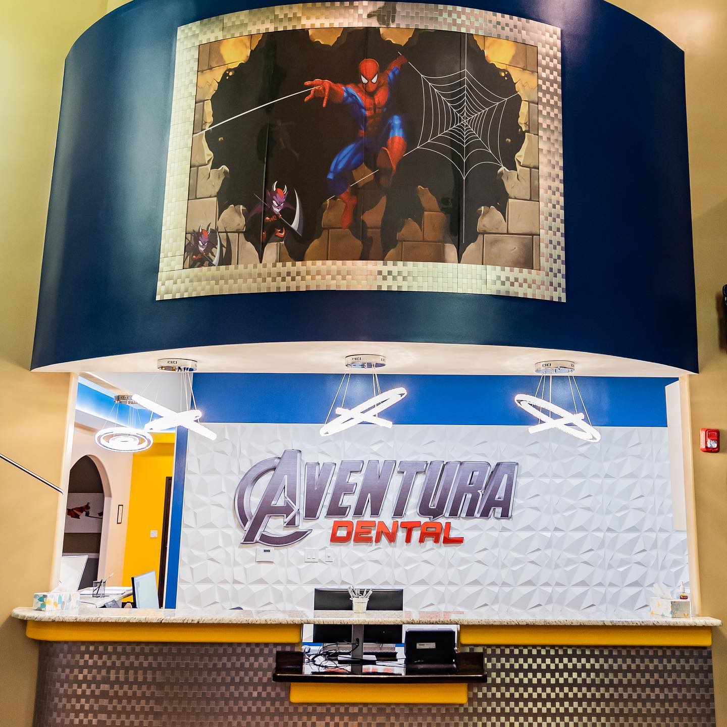 Aventura Dental reception with blue walls, white counter, and large Spider-Man mural overhead.