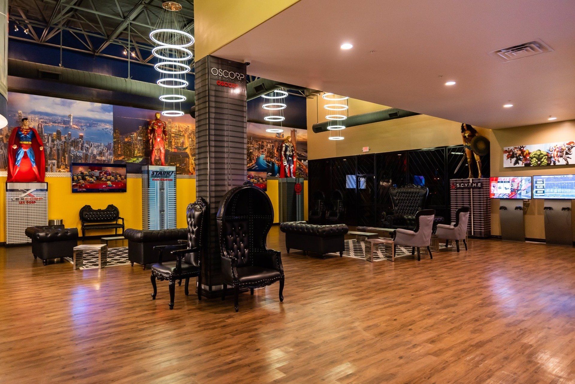 Spacious modern lounge with polished wood floor, black chairs, warm lighting, and a bar area in the background