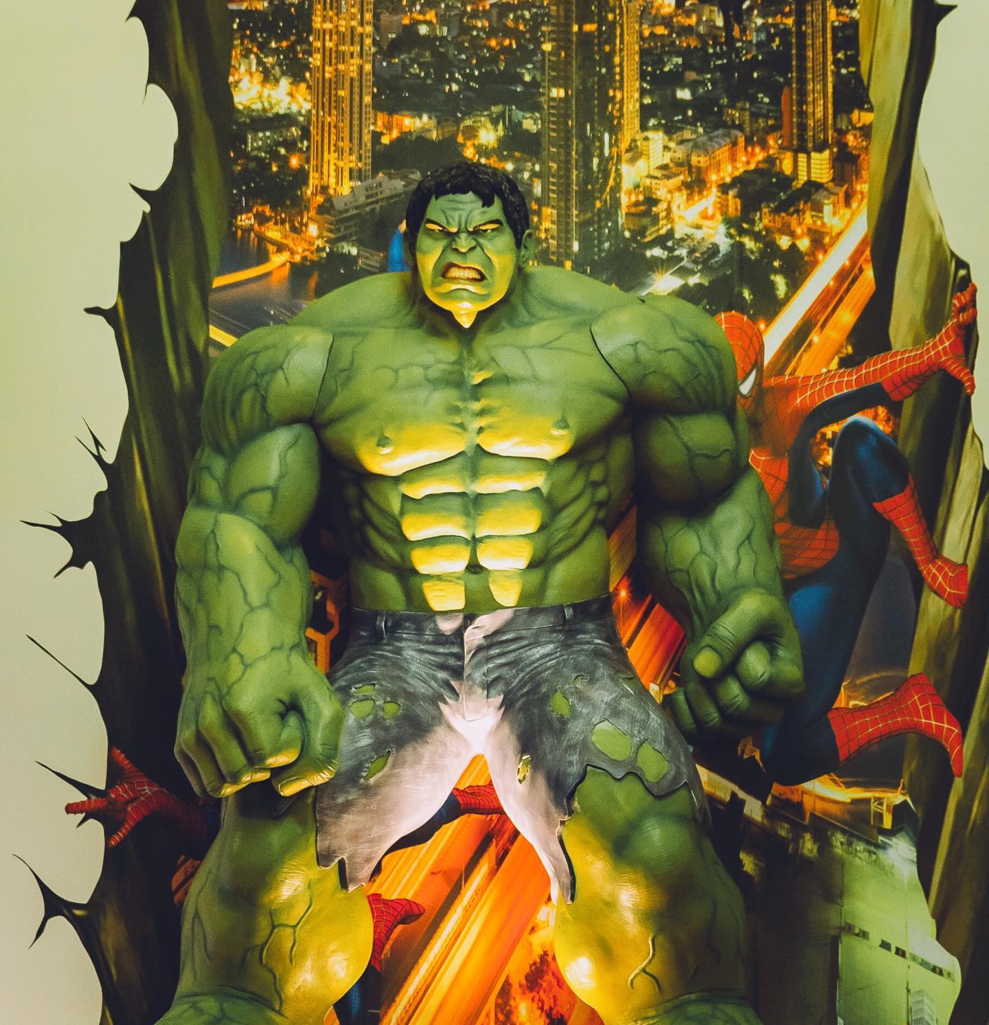 Green Hulk and Spider-Man amid a fiery city backdrop, bursting through a torn wall.