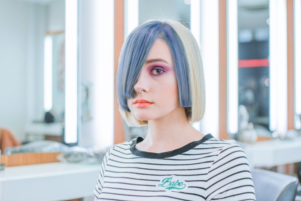 Woman with blue and blonde hair, wearing a striped shirt, in a salon.