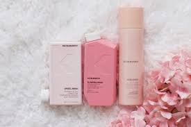 Three pink hair products on a fluffy white surface, next to pink flowers.