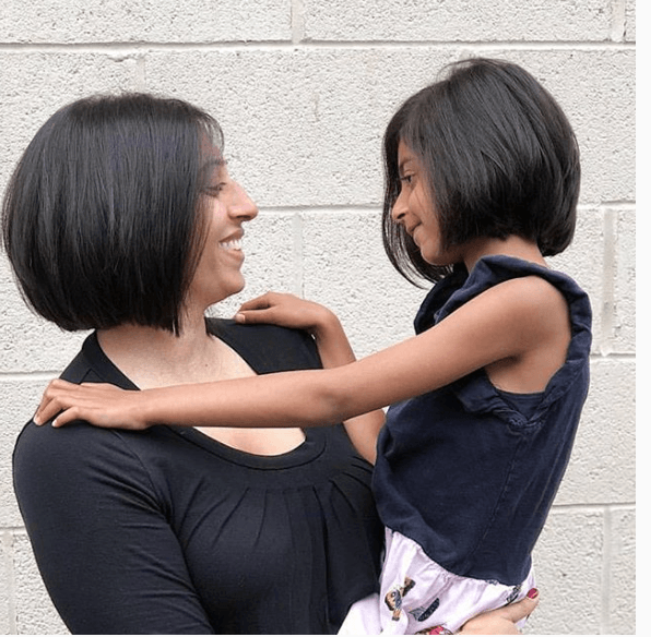 Woman and child smiling and embracing, in front of a brick wall.
