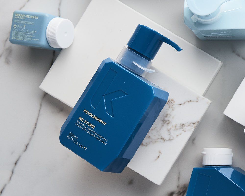 Blue shampoo bottle with pump on a marble surface, surrounded by other cosmetic products.