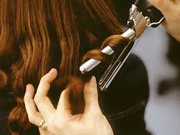 Person curling brown hair with a curling iron. Close up of hands and hair in action.