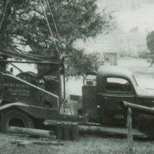 Black and white photo of a tow truck. The truck is parked outdoors near trees.