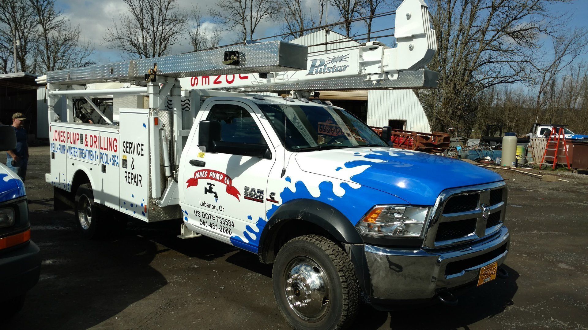 White and blue work truck with a raised boom, parked outdoors.
