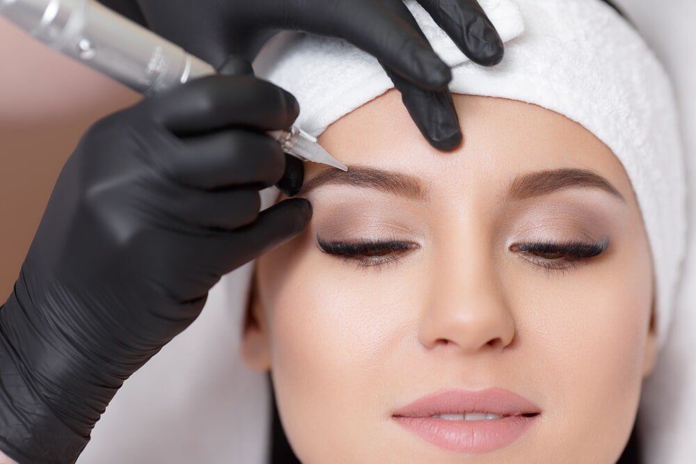 A woman is getting her eyebrows tattooed with a machine.