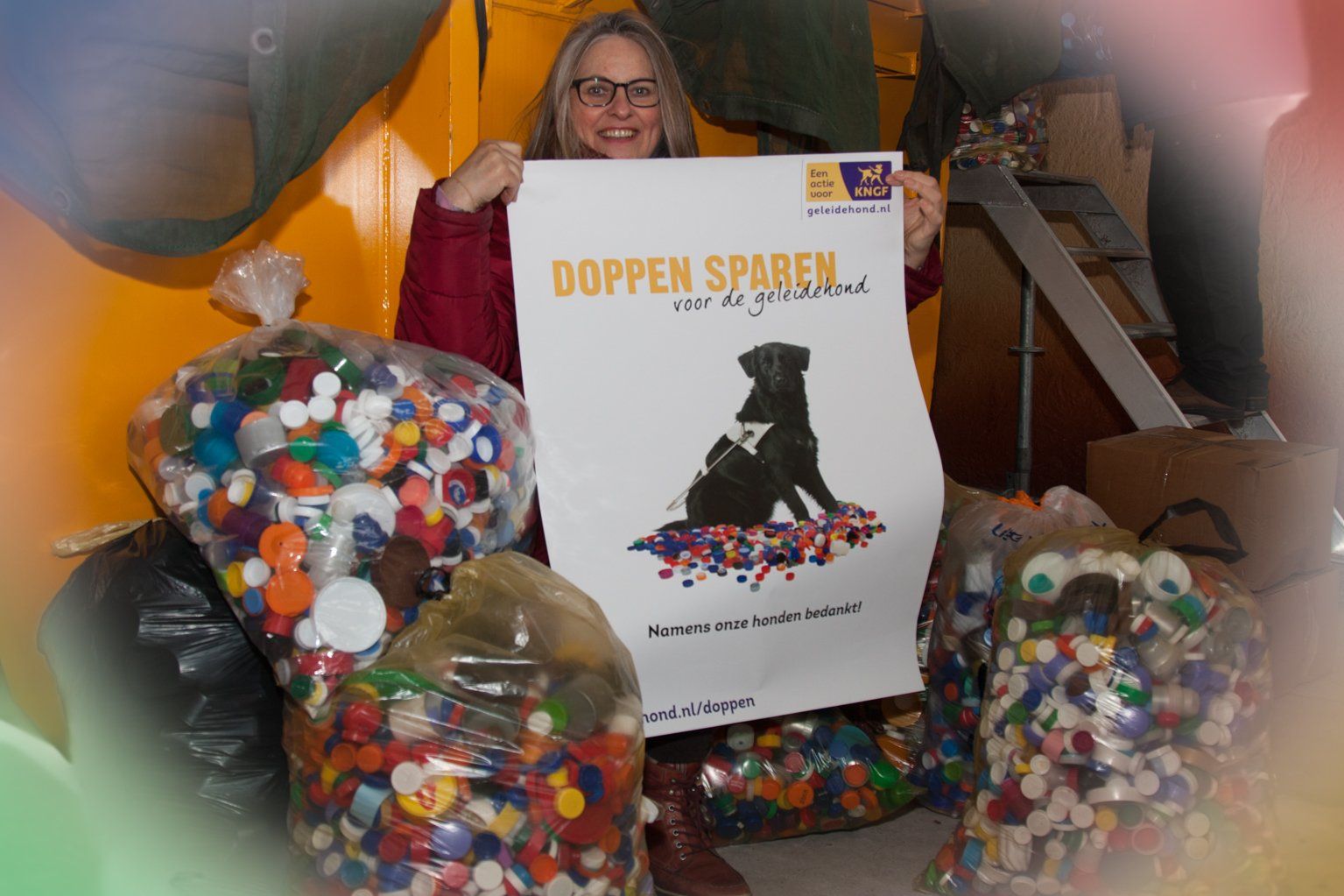 spaarder tussen 4 volle plastic zakken met plastic doppen en poster van doppenactie van het KNGF