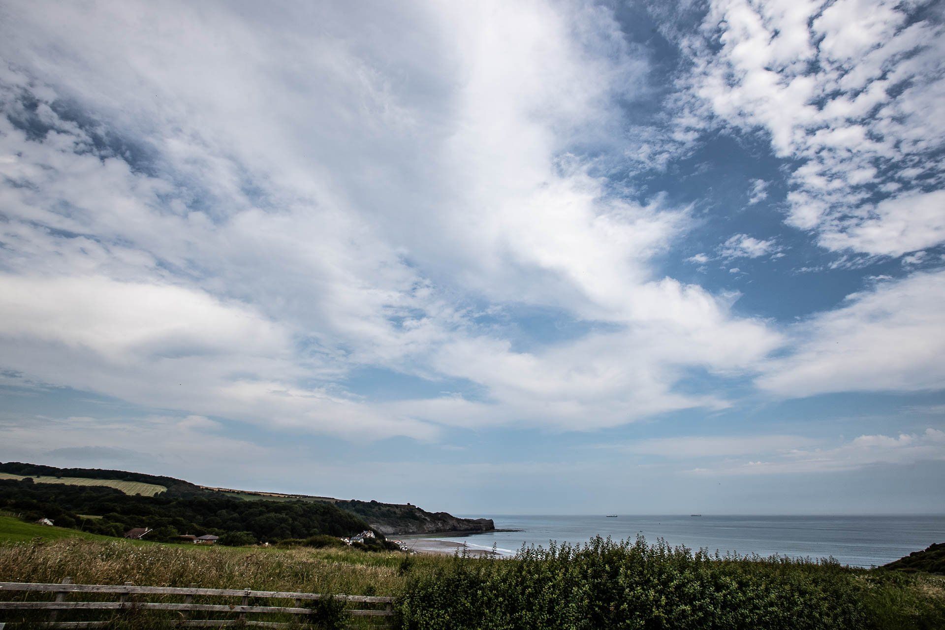 Blue sky with scattered clouds over a coastal scene with ocean, beach, and greenery.