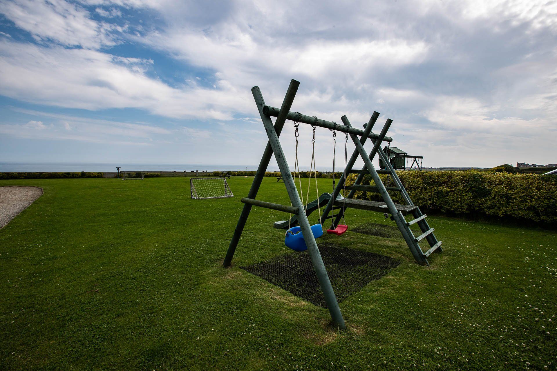 Playground swing set on green grass with blue sky and ocean view.