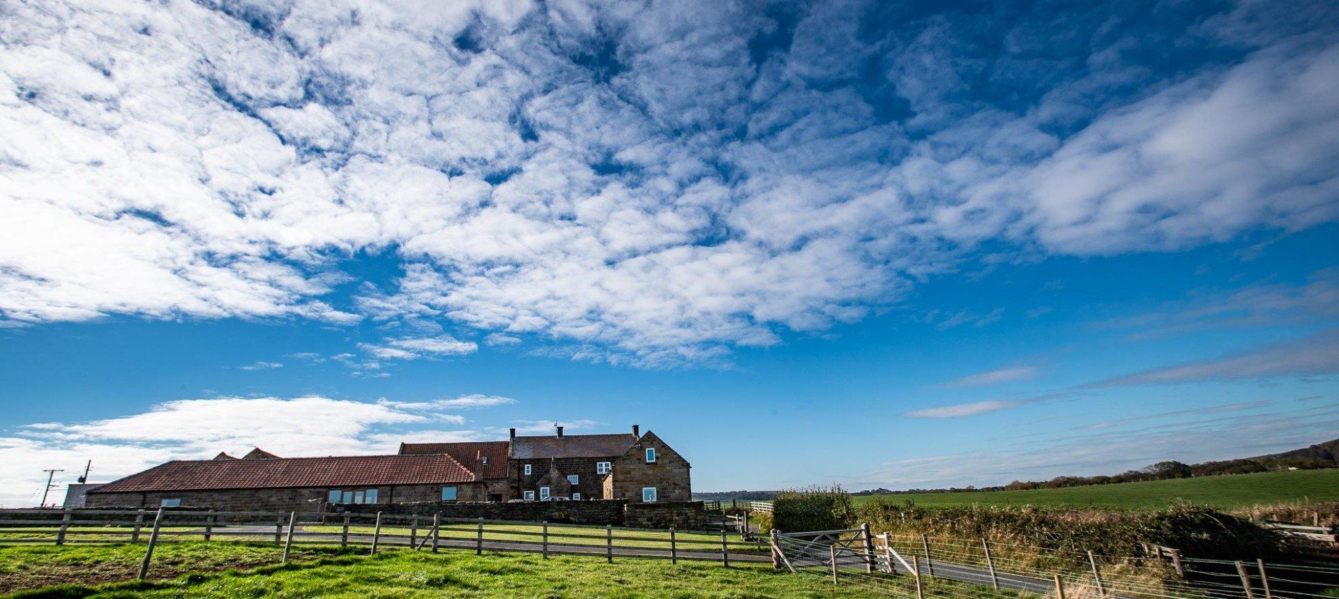 Farmhouse under a bright blue sky with white clouds, green field in front.