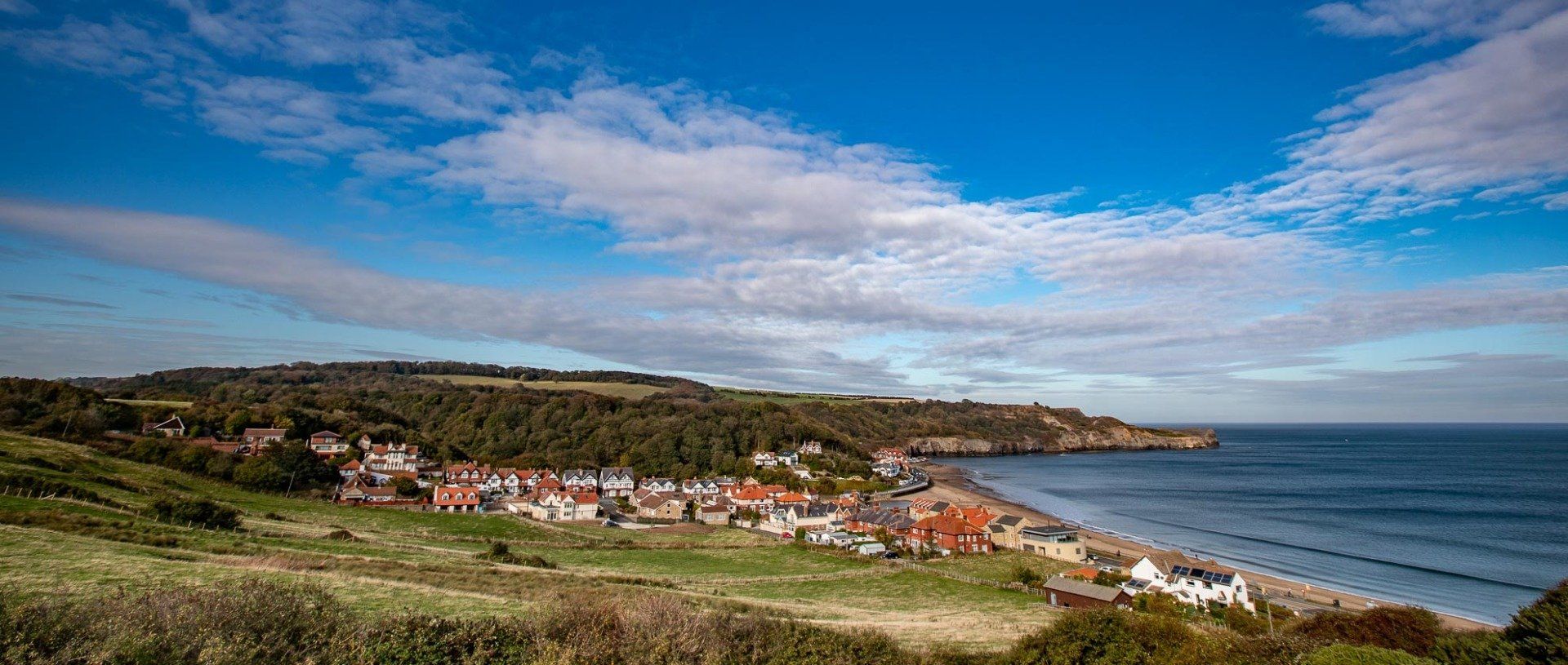 Coastal village with a sandy beach and calm blue sea under a partly cloudy sky.
