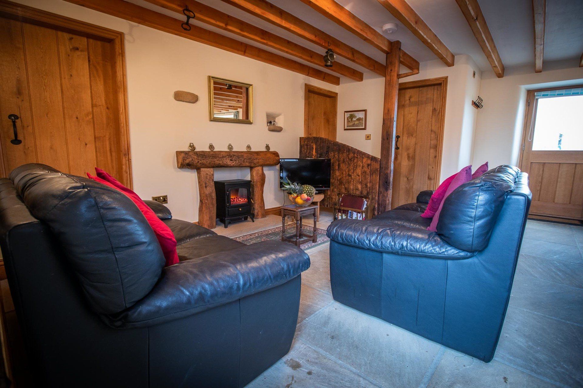 Cozy living room with black leather couches, a fireplace, and wooden beams.