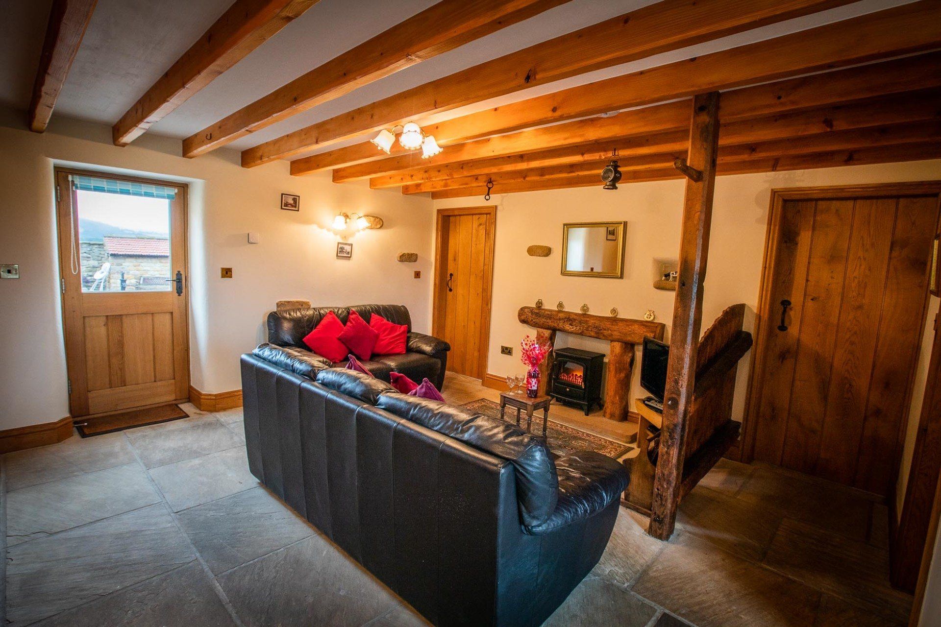 Cozy living room with black leather sofa, fireplace, wooden beams, and a stone floor.