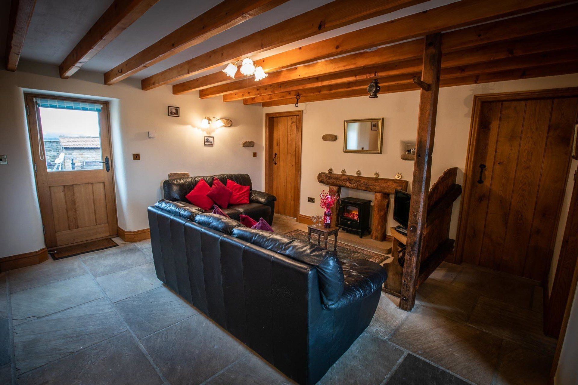 Living room with black leather sofas, fireplace, wooden beams, and stone floor.
