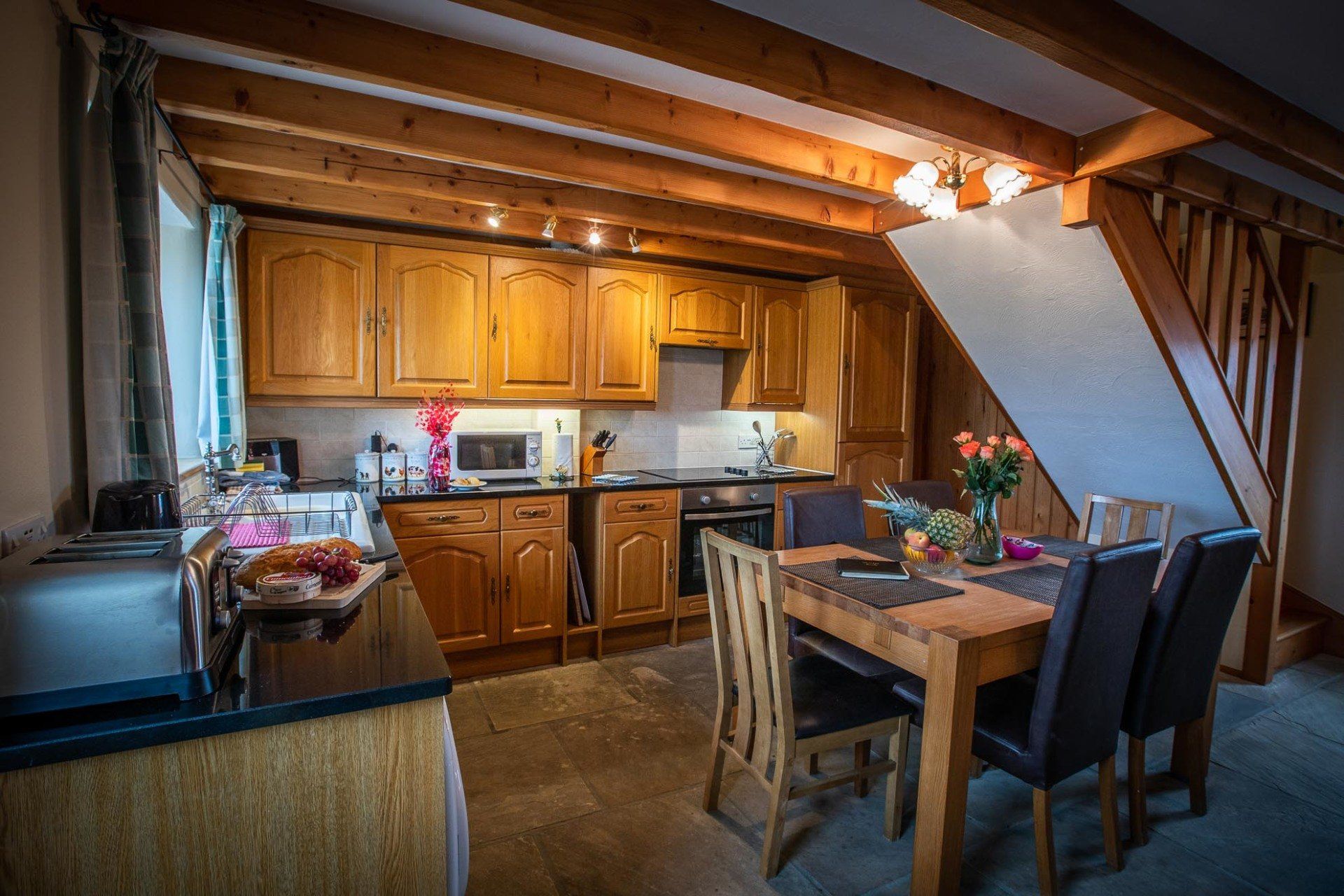 Kitchen with wooden cabinets, beams, and a dining table with chairs.