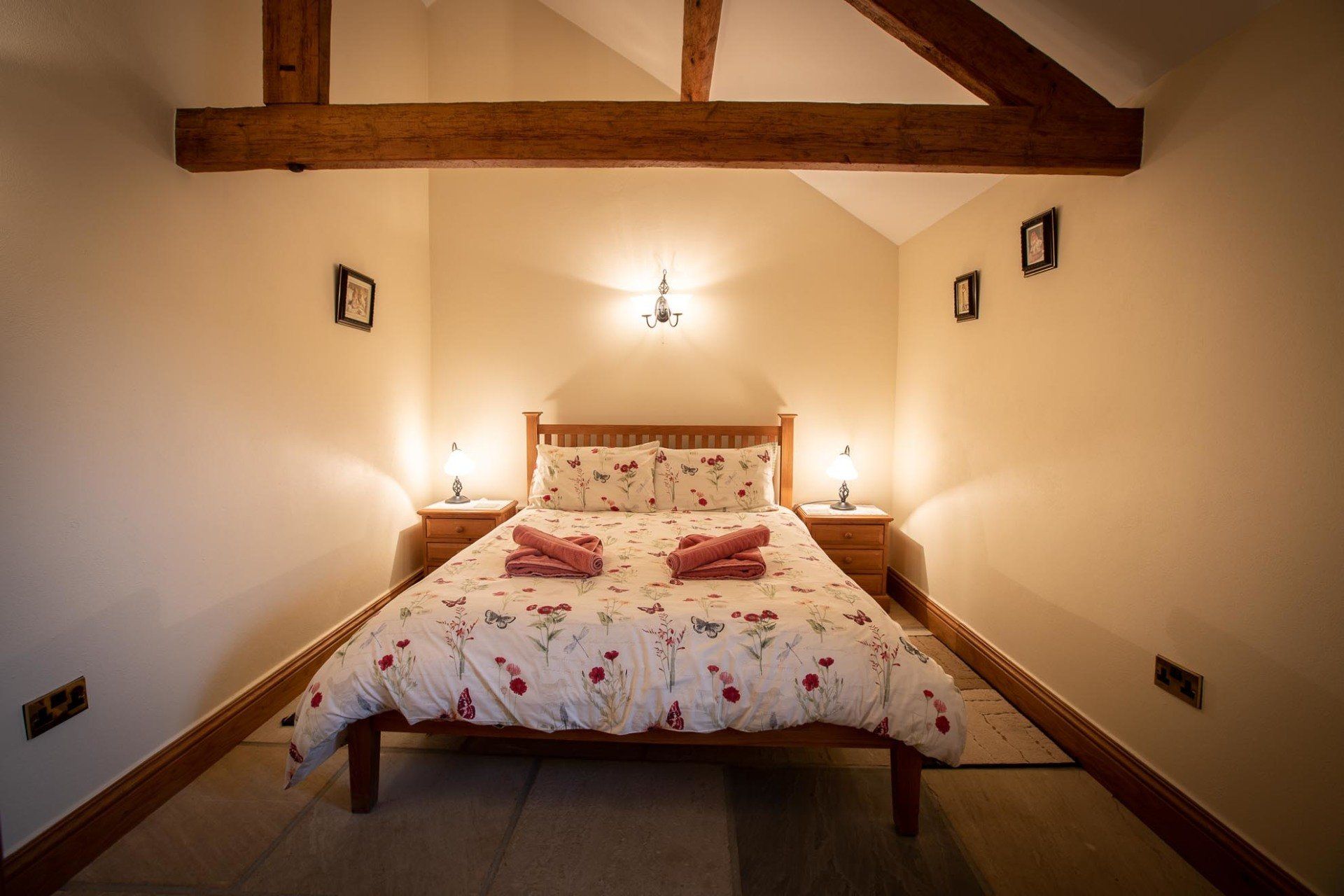 Bedroom with a wooden bed, nightstands, and floral bedding. Exposed wooden beams and sconce.