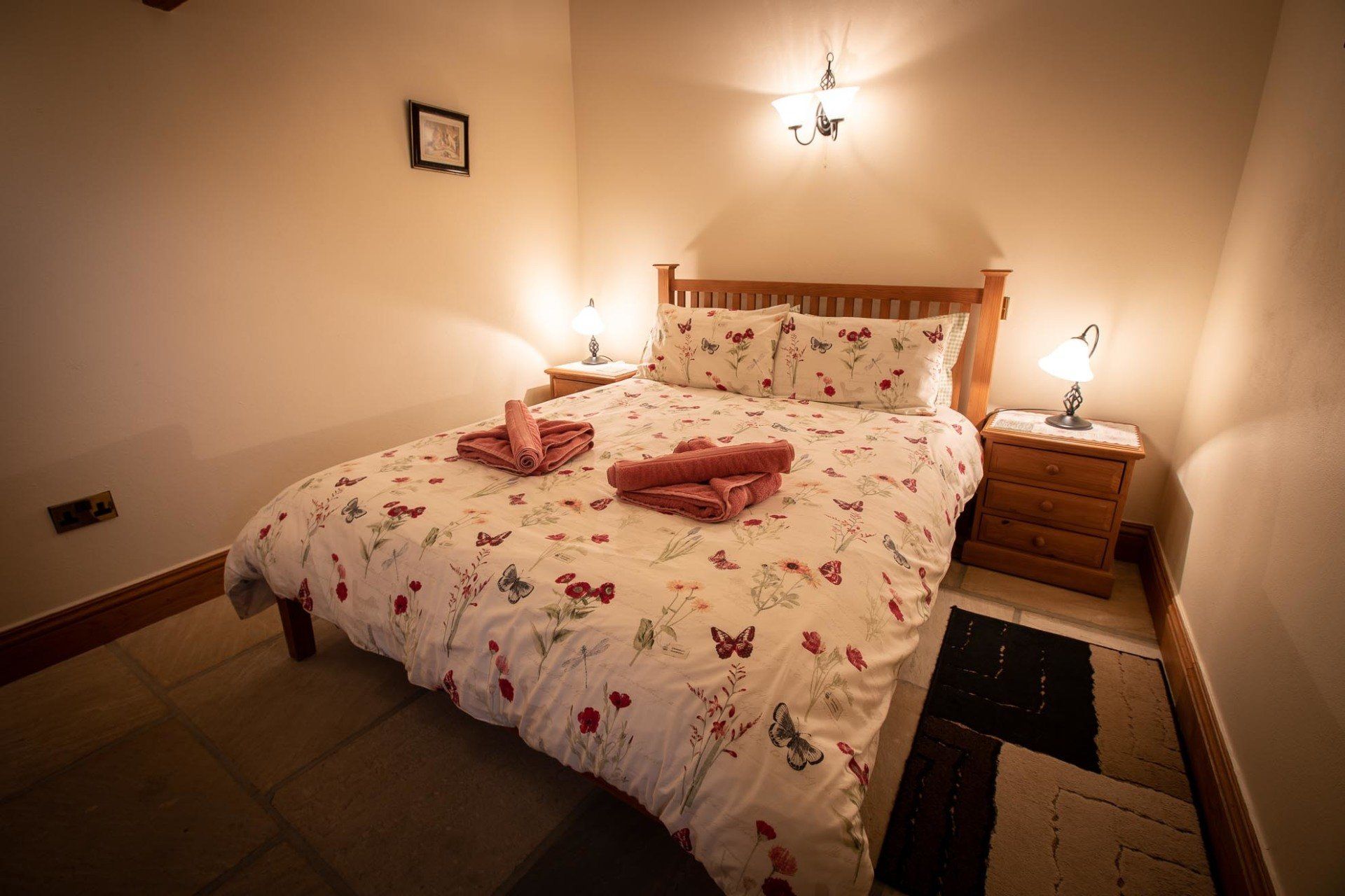 Cozy bedroom with double bed, floral bedding, two nightstands, lamps, and a small rug.