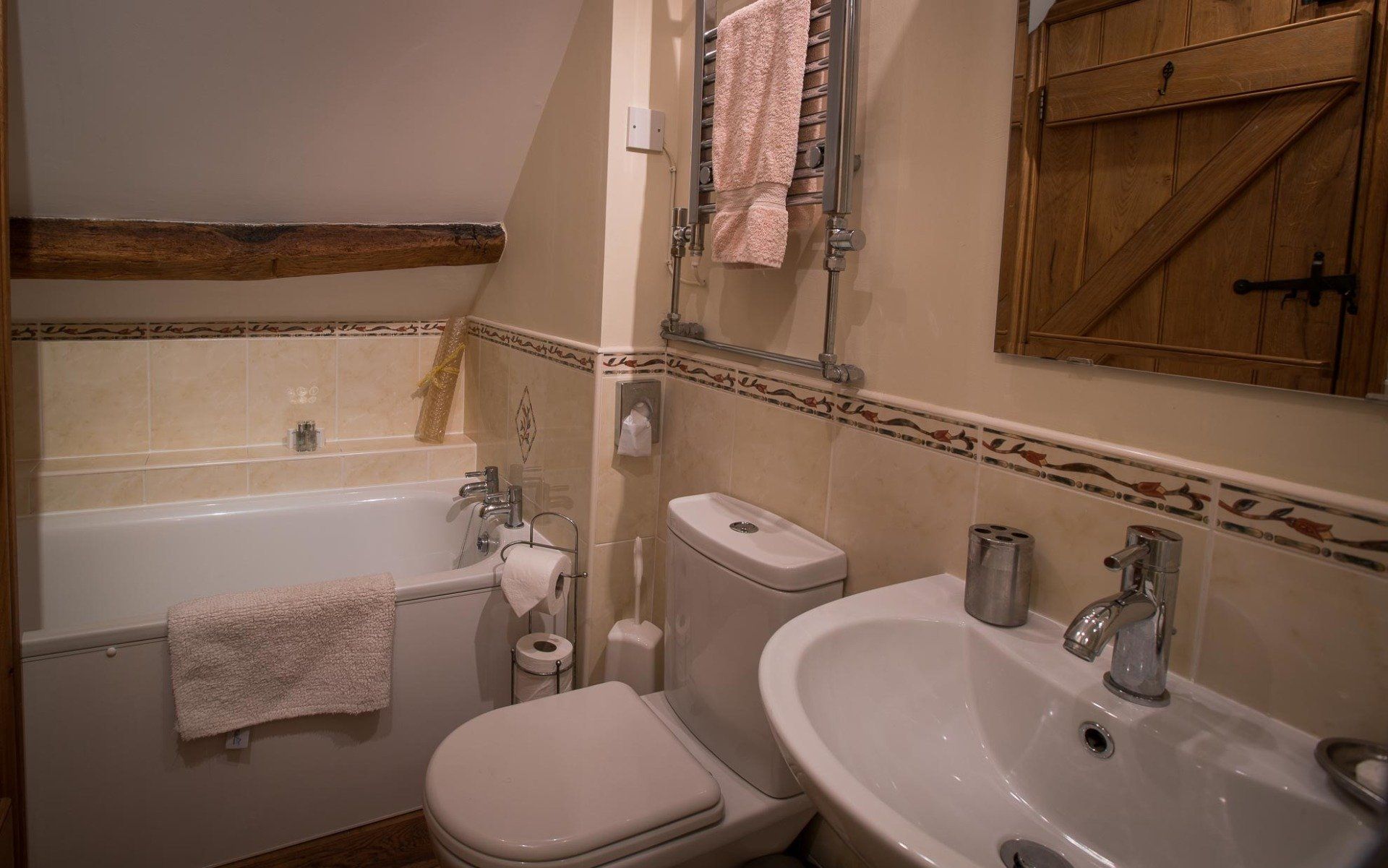 Bathroom with tub, toilet, and sink. Beige walls, wood accents, and a towel on the tub.