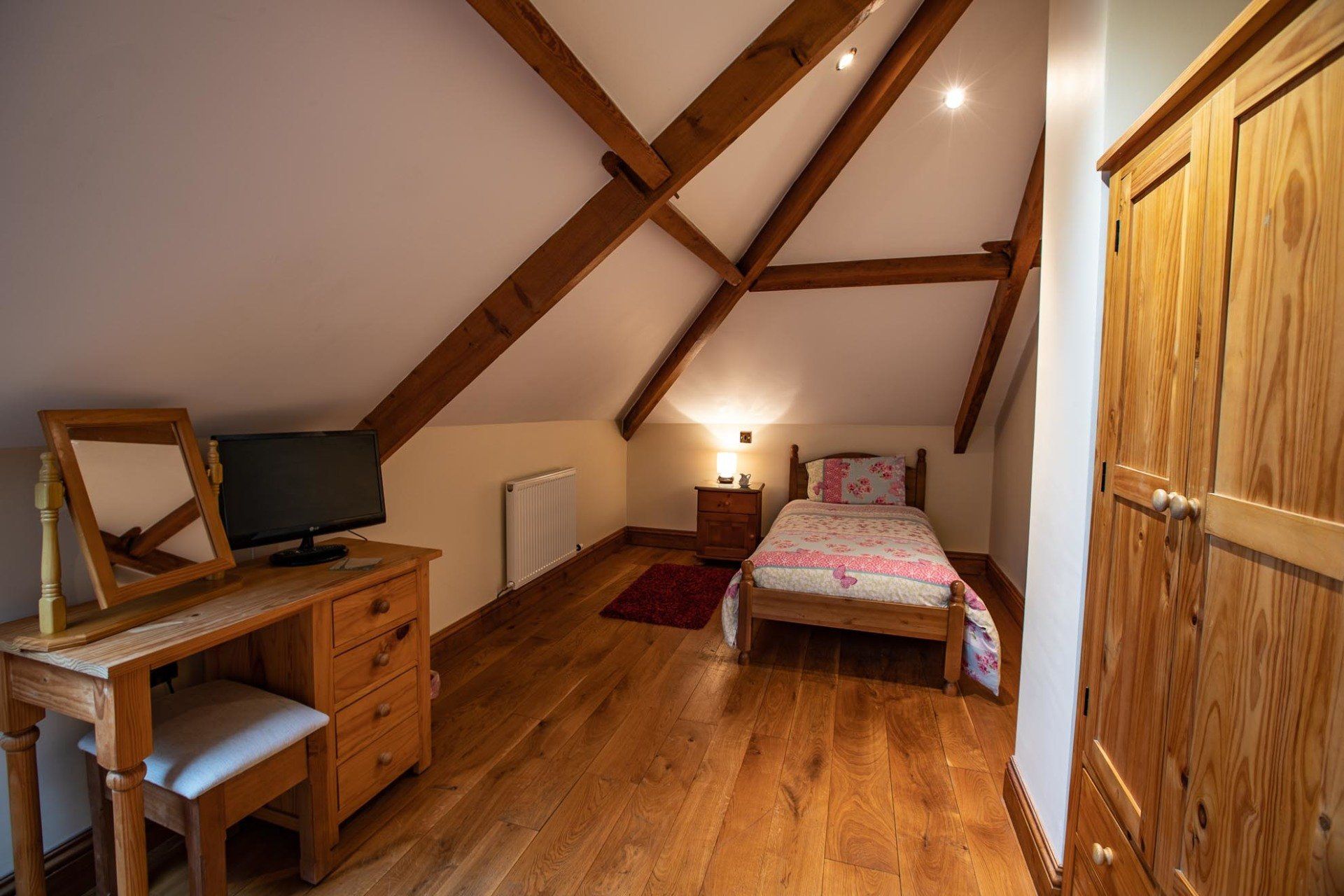 Bedroom with exposed wooden beams, single bed, dresser with mirror, wooden floor, and wardrobe.