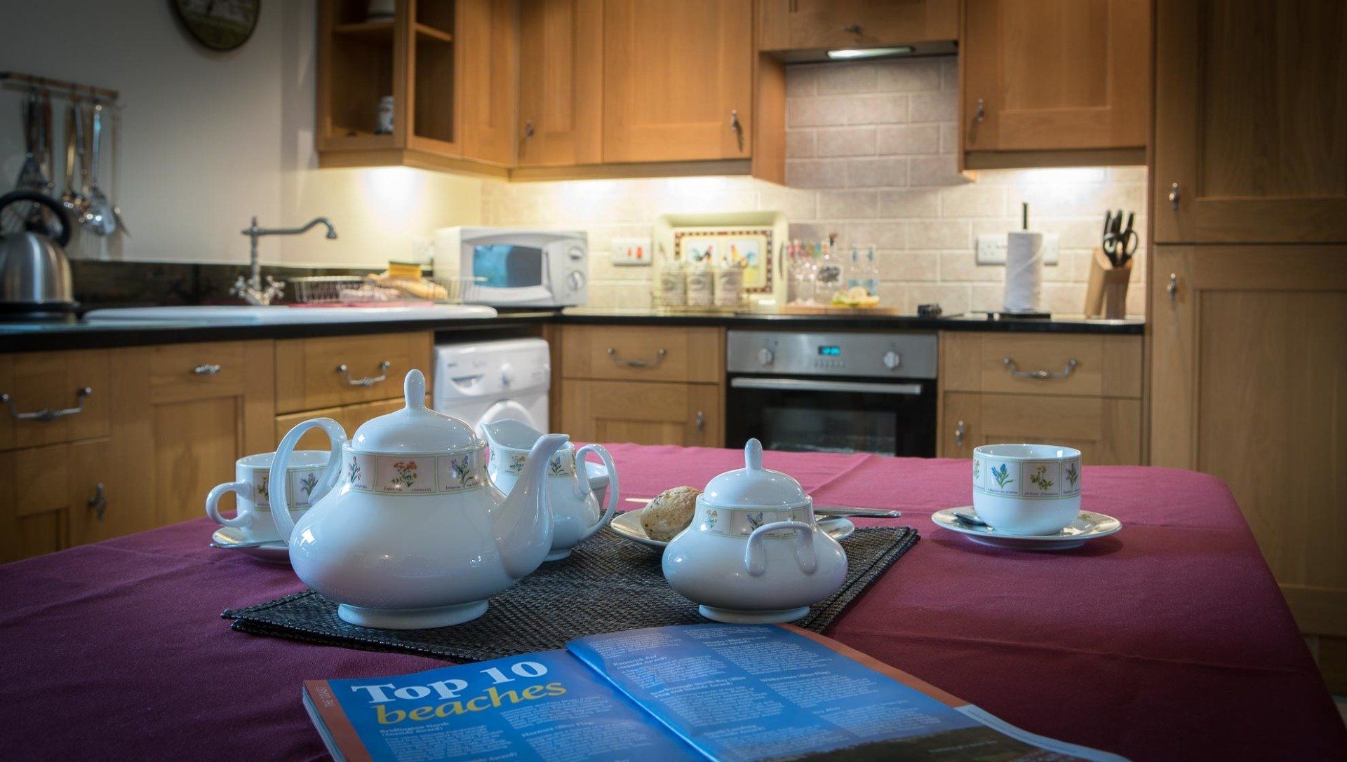 Kitchen with tea set on a table, including teacups, teapot, and sugar bowl, with a brochure.