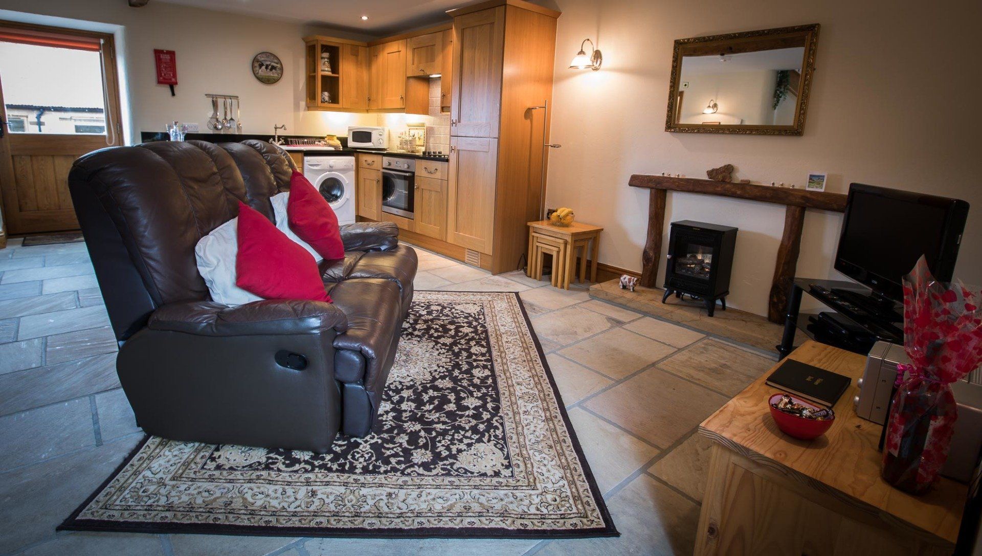Cozy living room with brown leather recliner, fireplace, rug, and small kitchen in the background.