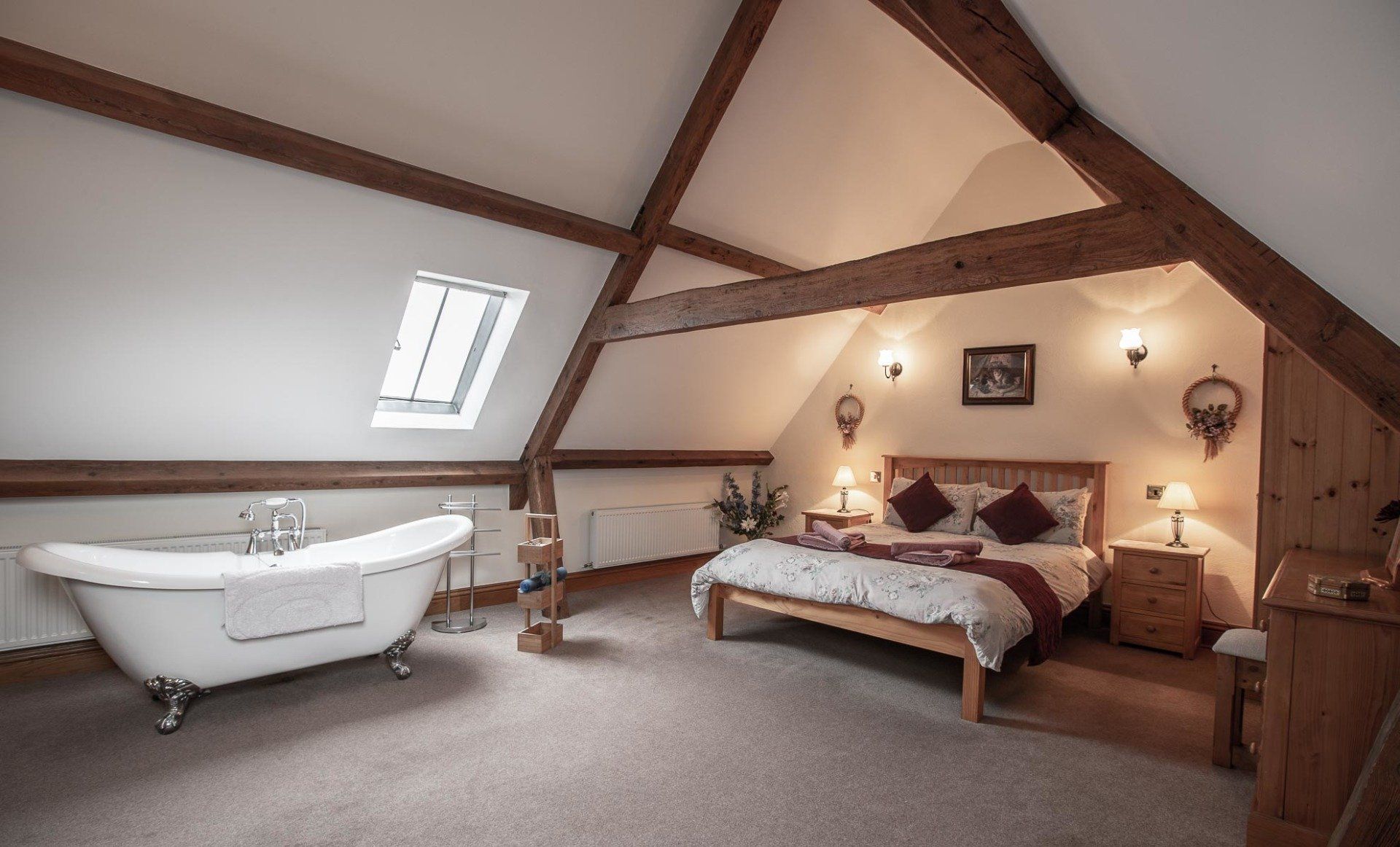 Bedroom with a clawfoot bathtub, wooden beams, a bed, and skylight.