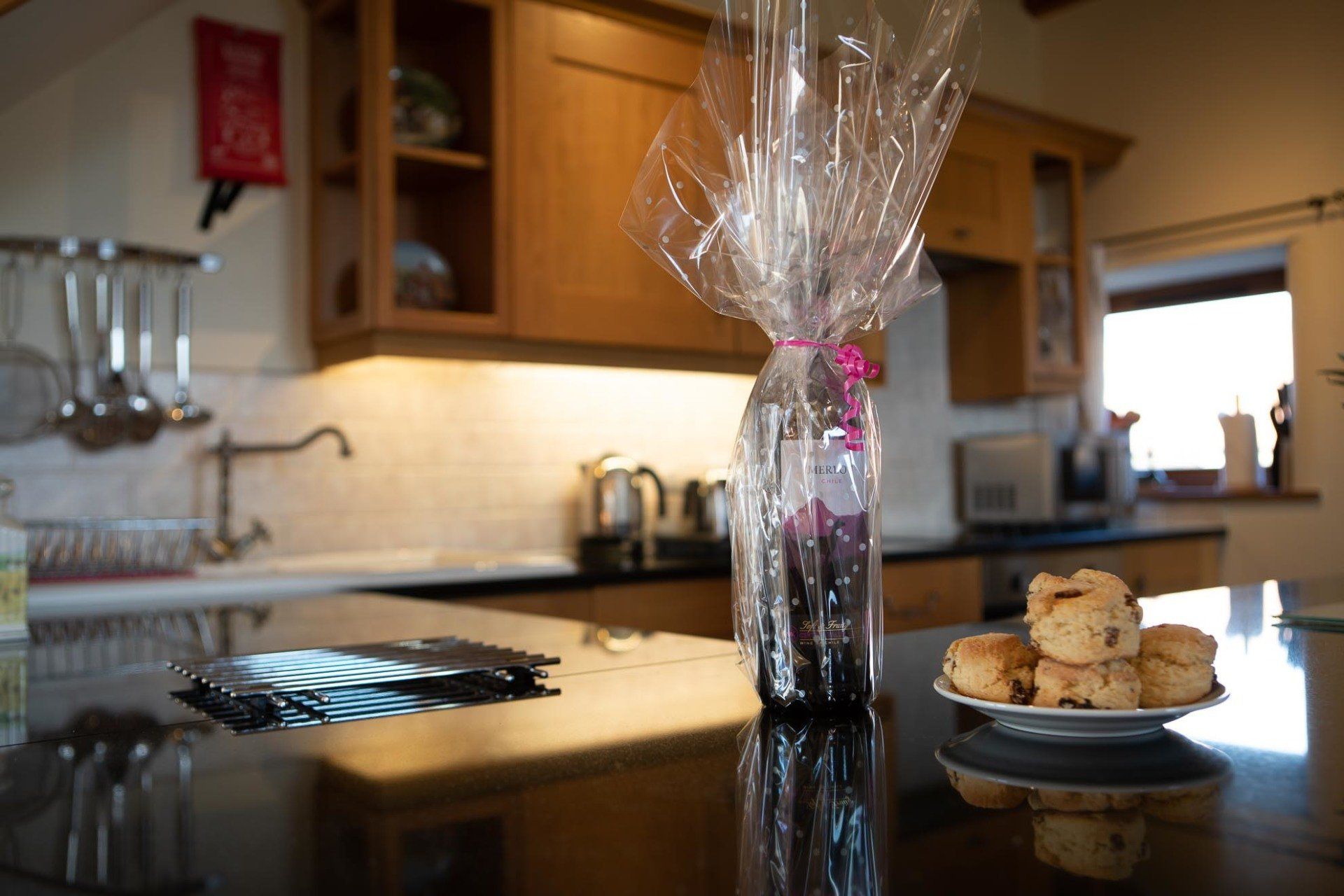 Kitchen counter with wrapped bottle, plate of scones, and cabinets in the background.