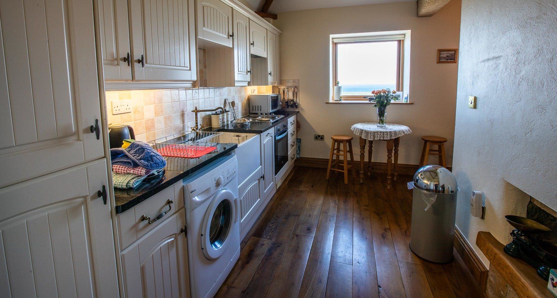 Kitchen with white cabinets, appliances, small table, stools, and window with view.