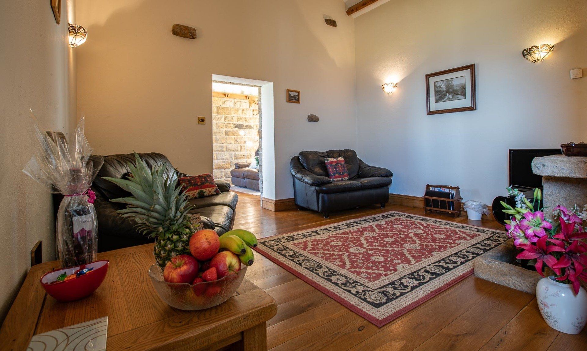 Living room with leather furniture, fruit, rug, and doorway to a stone-walled room.