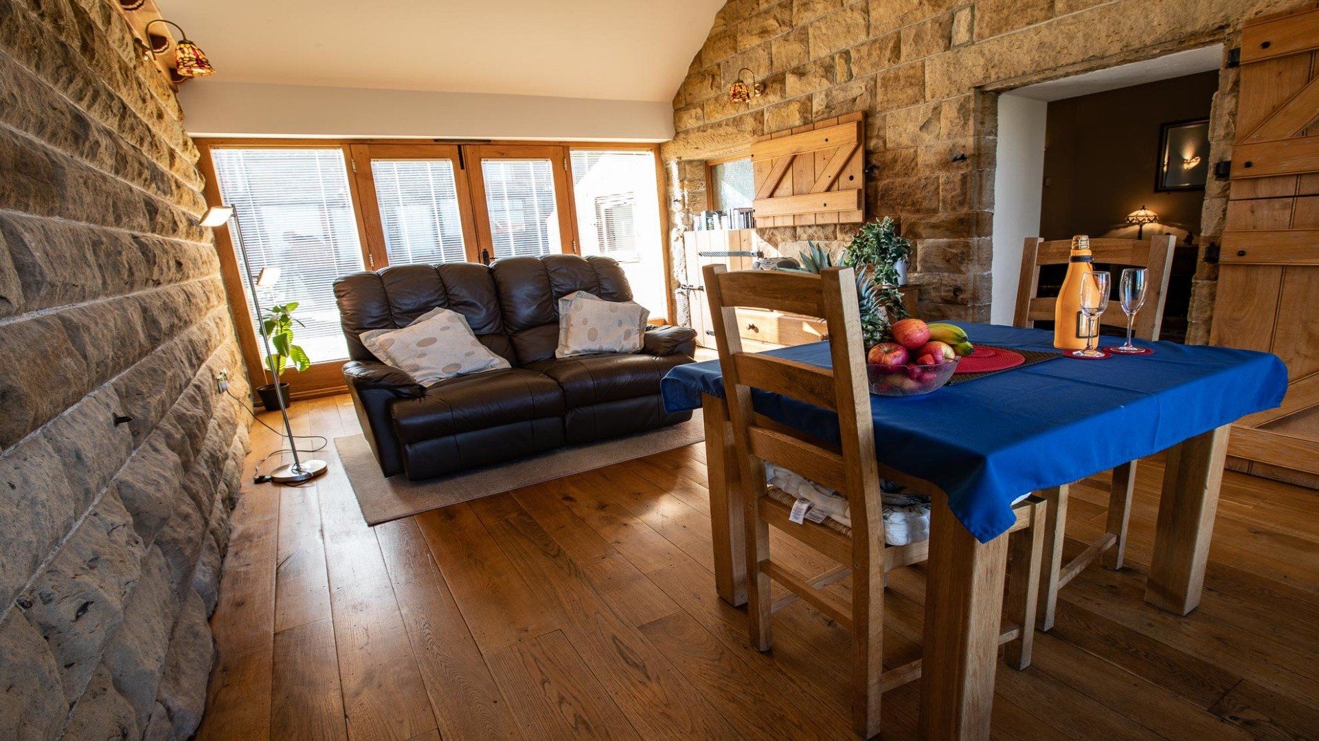 Cozy interior with a leather sofa, wooden table set for dinner, and stone walls.
