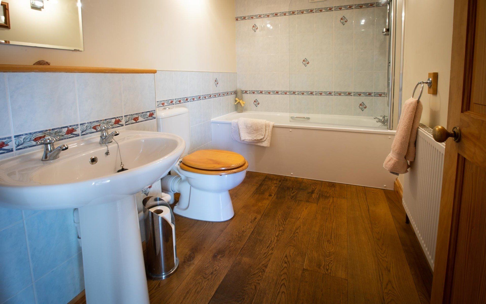 Bathroom with a white sink, toilet, bathtub, shower, and wooden floors.