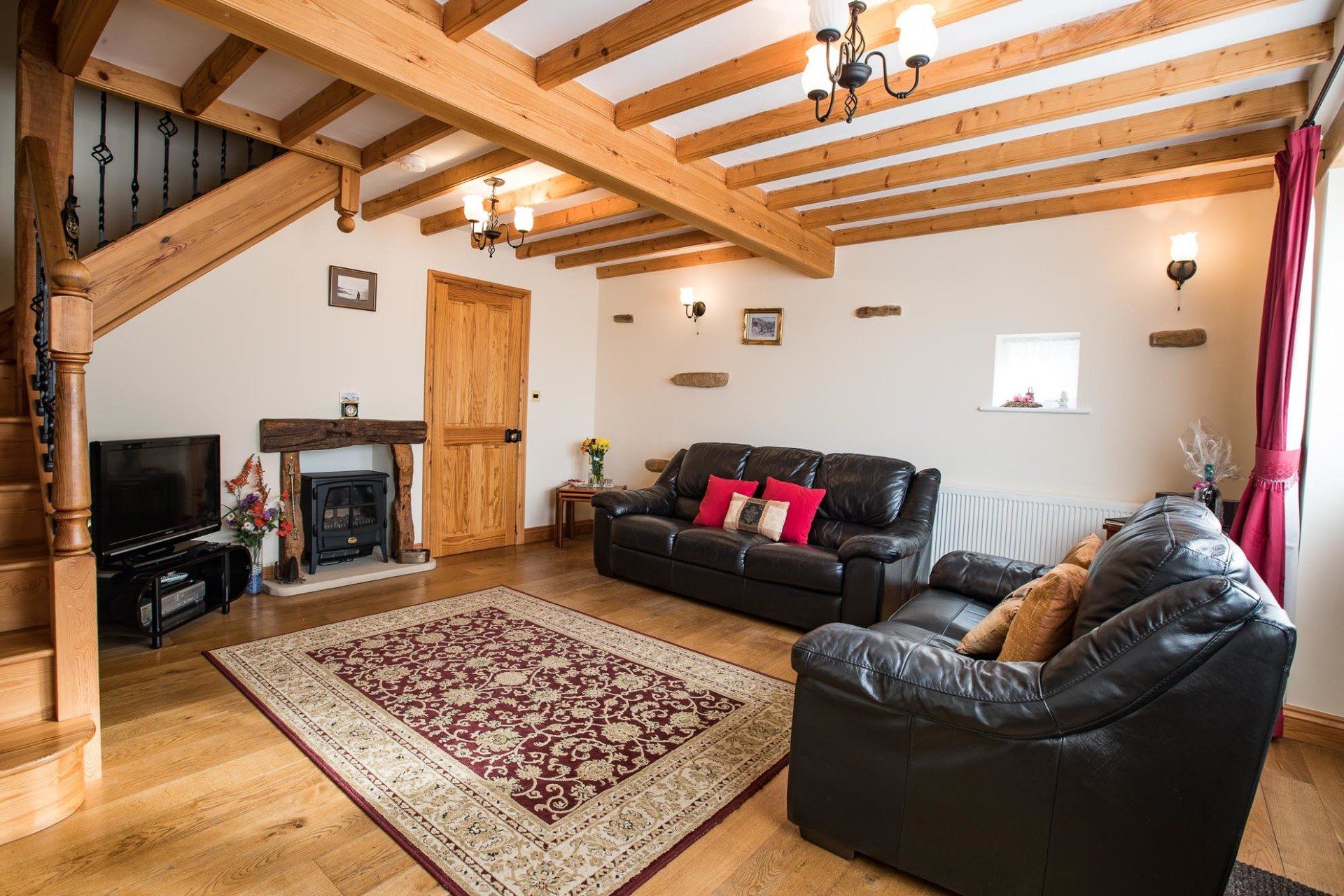 Living room with exposed wooden beams, fireplace, and leather sofas.