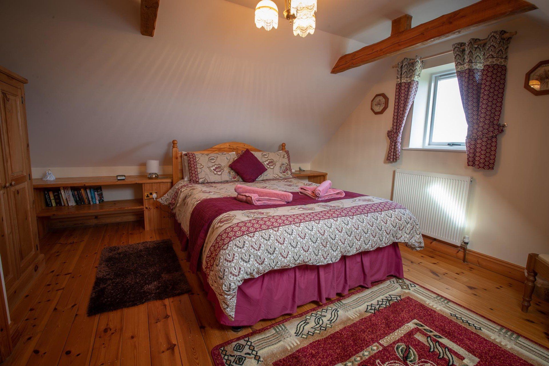 Bedroom with a bed, wooden floor, and a window with curtains.