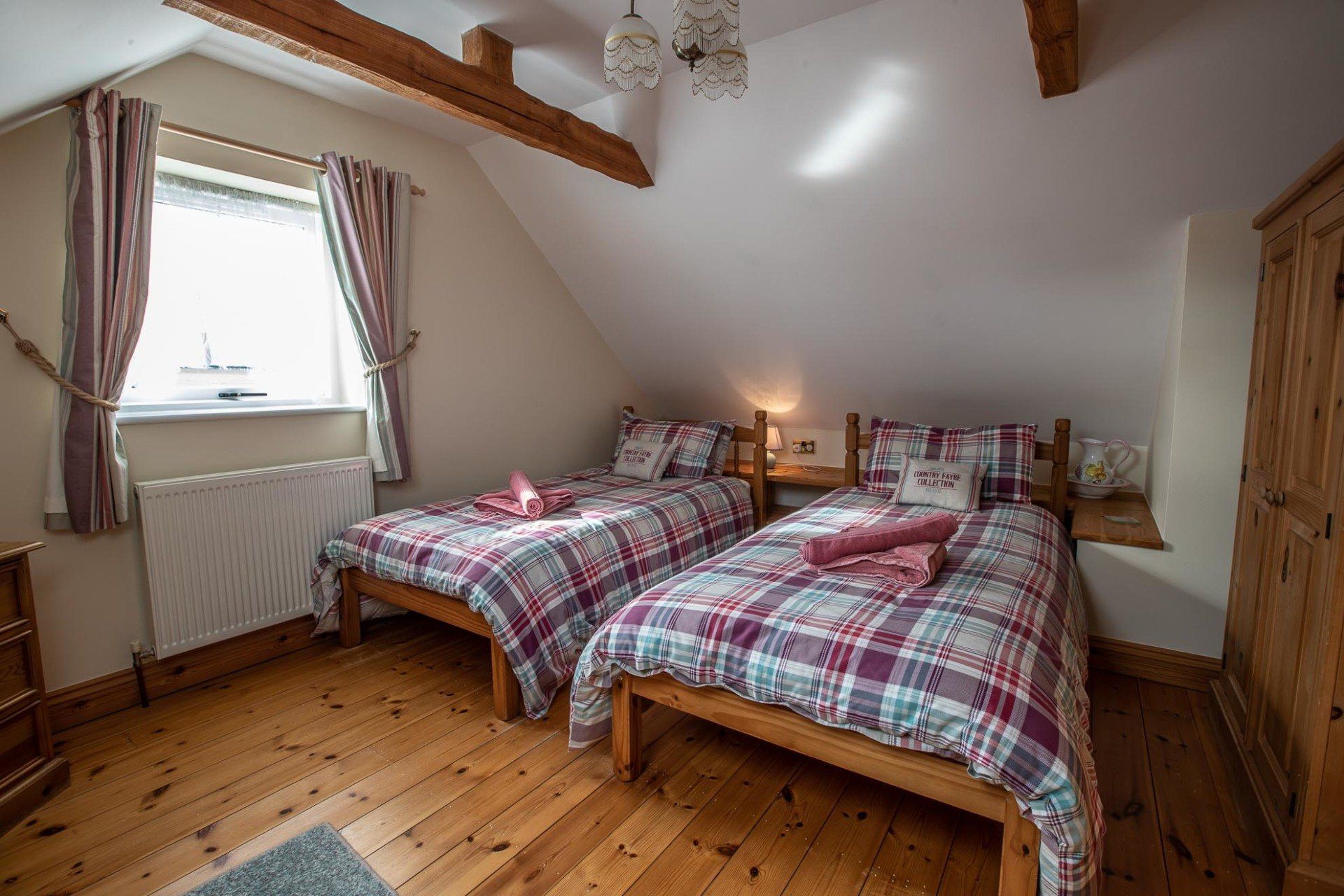 Bedroom with two twin beds, plaid bedding, window with curtains, and wooden floor.