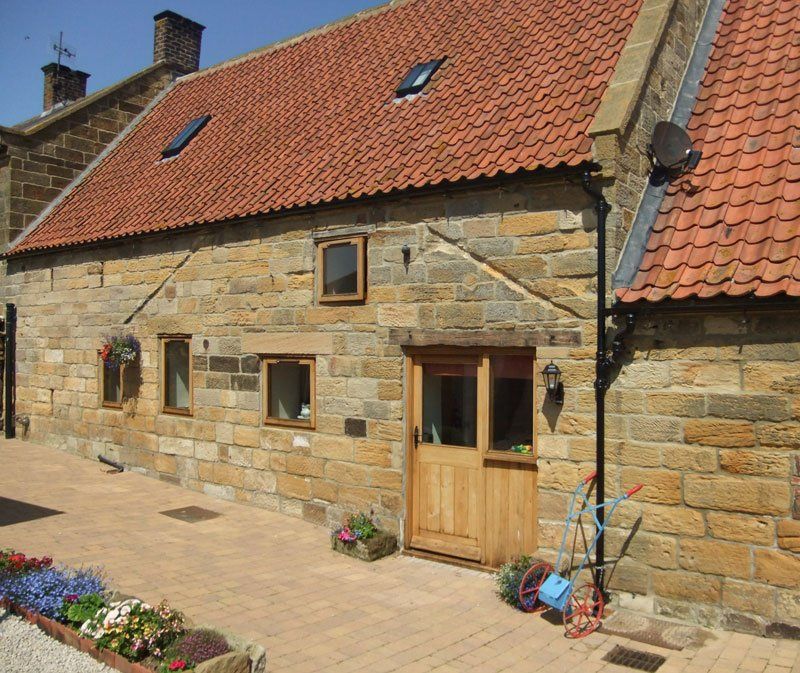 Stone cottage with red tiled roof and wooden door, small windows, and flower boxes outside.
