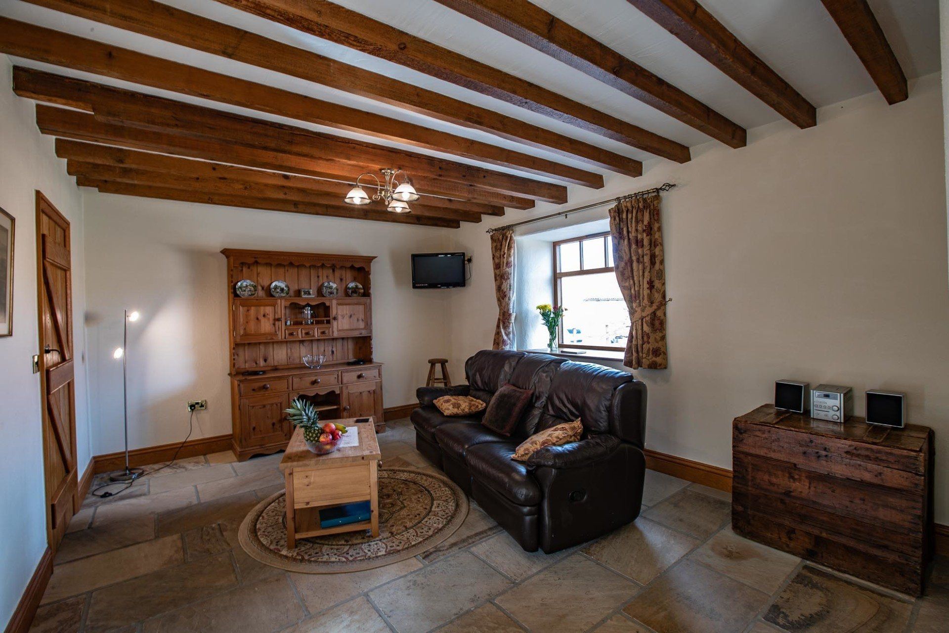 Living room with leather sofa, wooden beams, stone floor, and antique furniture.