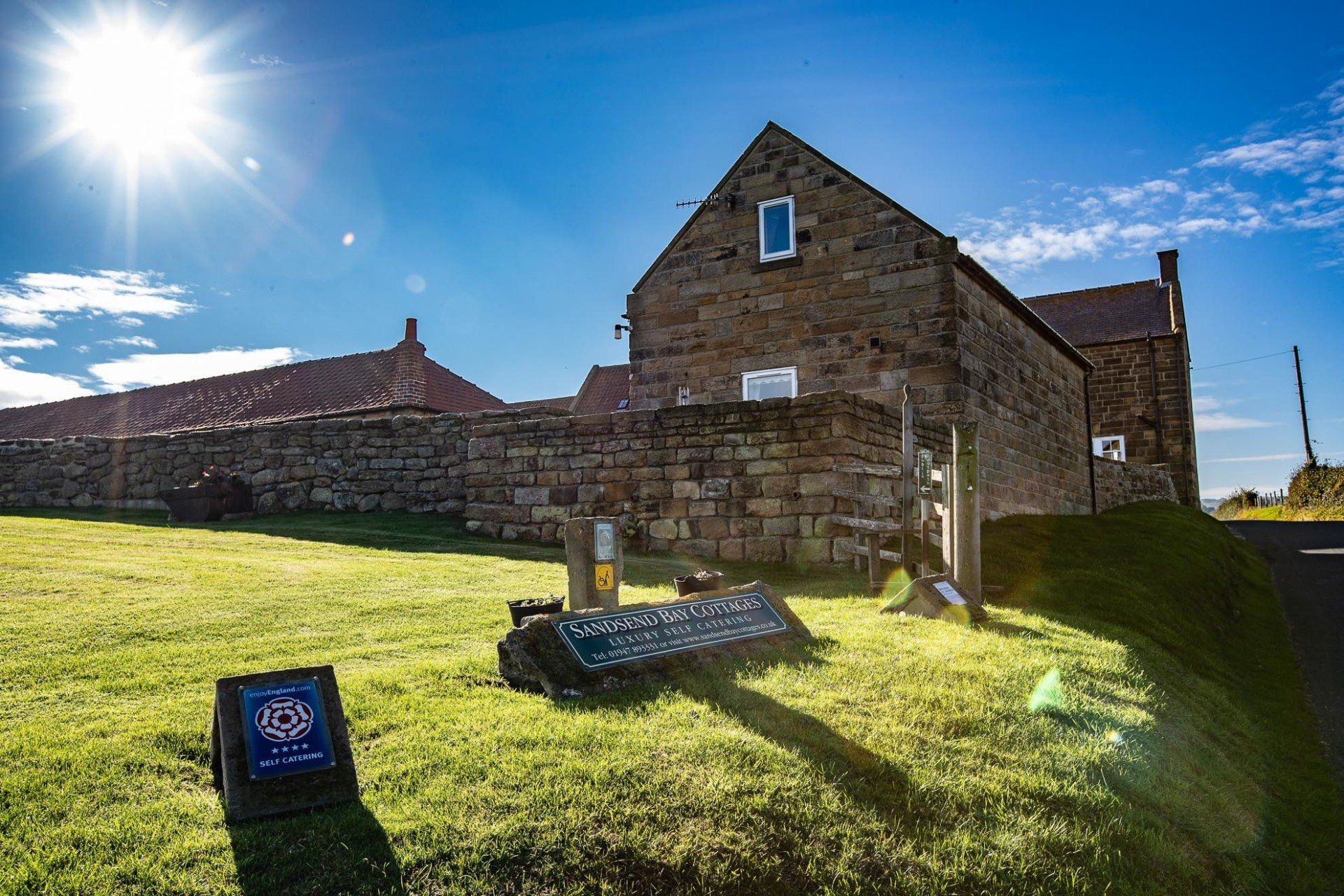 Sunny day shot of stone buildings with a grassy foreground and blue sky.
