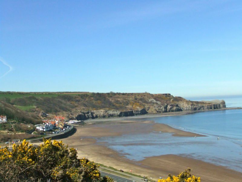 Coastal view: beach, cliffs, buildings, and blue sky.