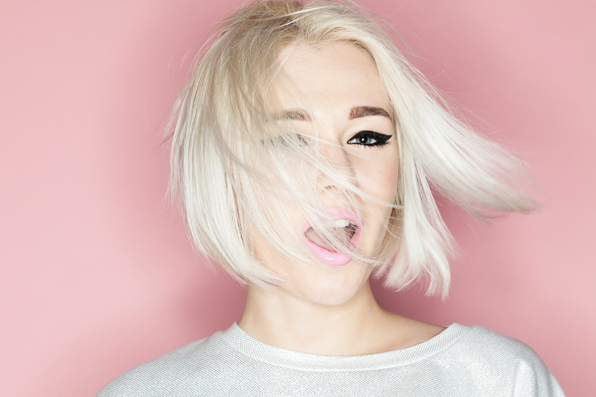 A woman with blonde hair is making a funny face with her hair blowing in the wind.
