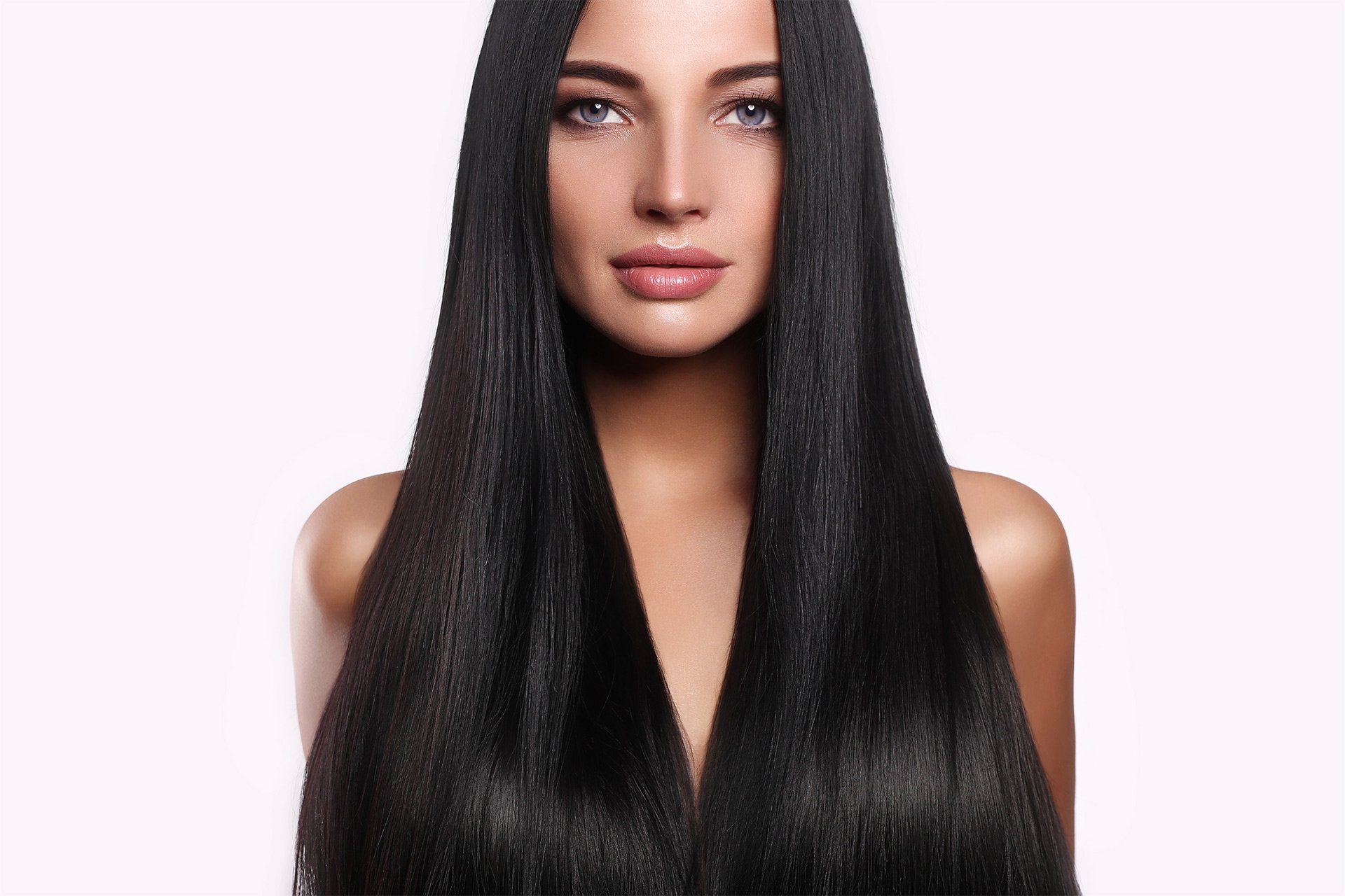 A woman with long black hair is standing in front of a white background.
